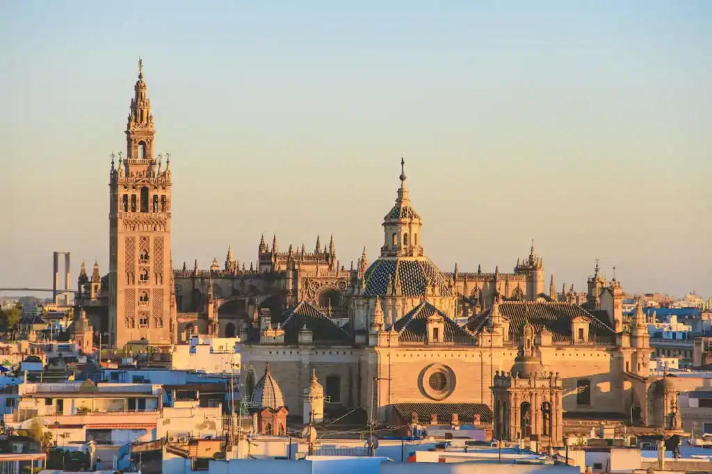Panoramic rooftop view of the Seville Cathedral and Giralda bell tower during a golden hour sunset in Seville, Spain, presented by Baraka Trios.