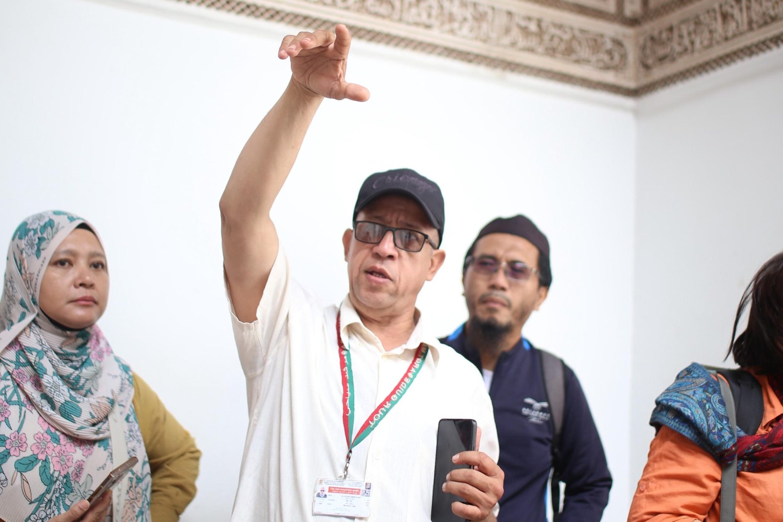 "A professional local guide from Baraka Trips explaining historical details to a group of attentive travelers inside a Moroccan monument with traditional architectural carvings."