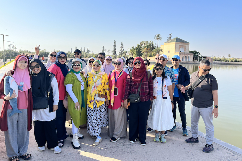 "A happy group of travelers posing in front of the historic pavilion and reflecting pool at Menara Gardens in Marrakech, Morocco, during a Baraka Trips guided tour."