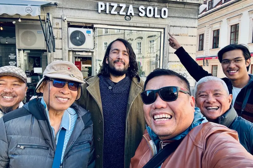 A group of cheerful travelers taking a selfie with their Baraka Trips guide in front of a local eatery, enjoying the social and authentic side of a private tour in Morocco.